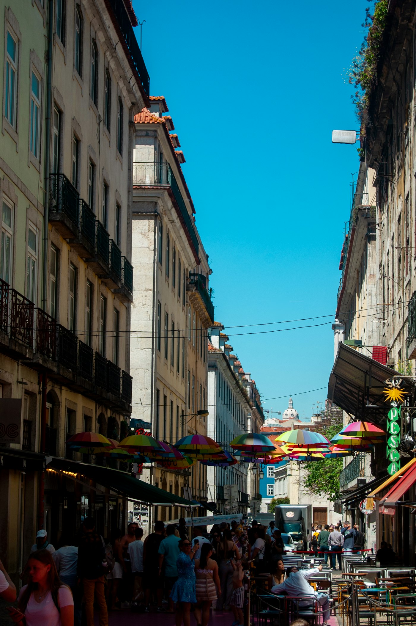 A busy tourist street lined with colorful umbrellas overhead